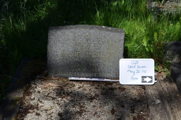 A photo of a gravestone. This photo contains a whiteboard with plot number, a north arrow, and a scale bar. There are some shadows on the stone.