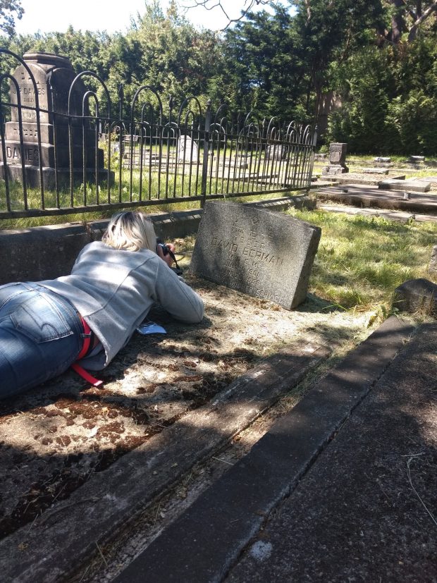 A photograph of a student lying prone and taking a photograph of a gravestone.