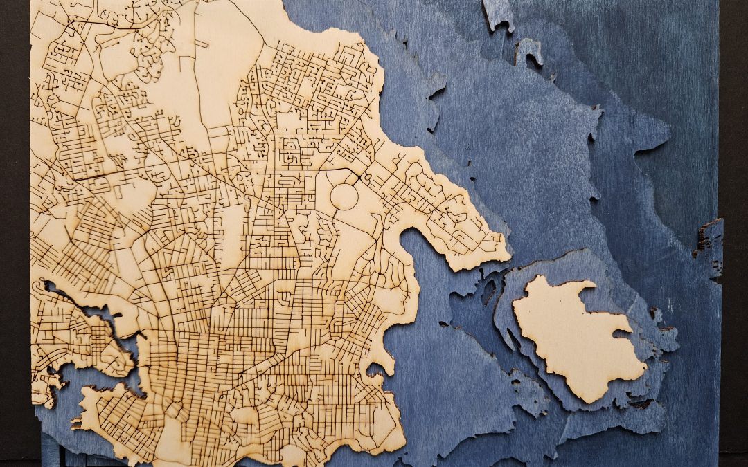 A laser cut map of Victoria, BC, with the streets engraved. The ocean is represented through stacked layers, coloured in blue that gets darker with increased depth.