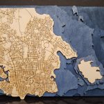 A laser cut map of Victoria, BC, with the streets engraved. The ocean is represented through stacked layers, coloured in blue that gets darker with increased depth.