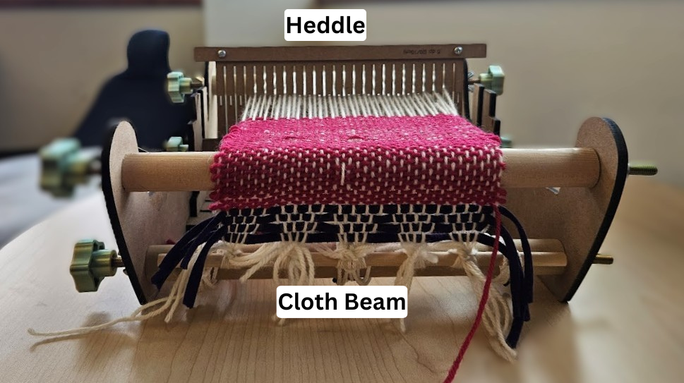 A wooden loom threaded with white and red yarn sitting on a table 