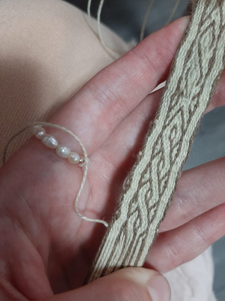 In this image I am holding my weaving. At the top of the band you can see a clear pattern that is not quite what I was aiming for but at the bottom you can see the completed pattern.