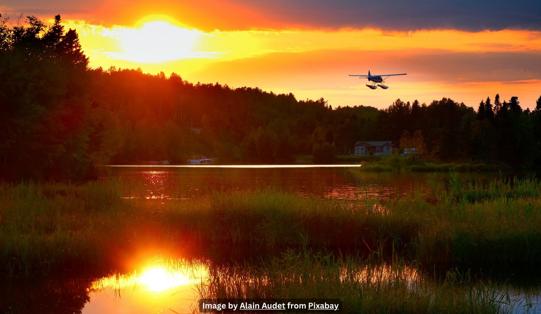 Swampy march at sunset with a small float plane flying over head. A house is in the distance.