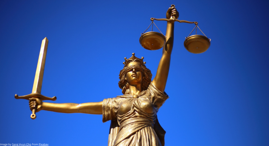A golden statue of Lady Justice holds balanced scales in one hand and a sword in the other, against a clear blue sky.