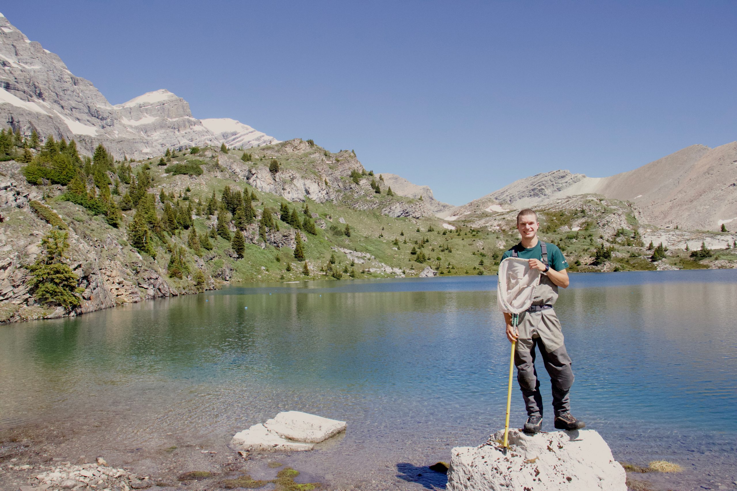 student holding dip net standing on shore of alpine lake