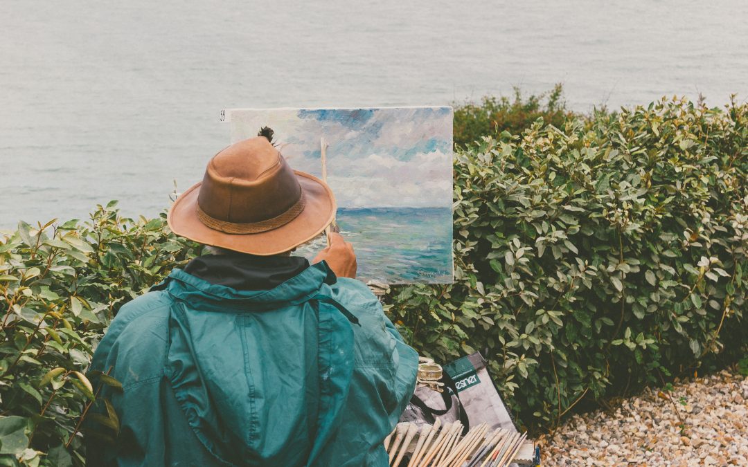 Person painting picture in front of ocean.