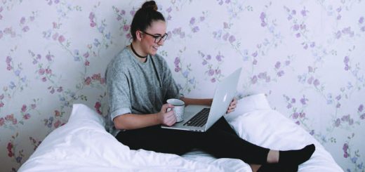 student holds a laptop and sites on a bed
