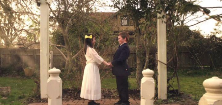 Two kids stand holding hands in wedding outfits