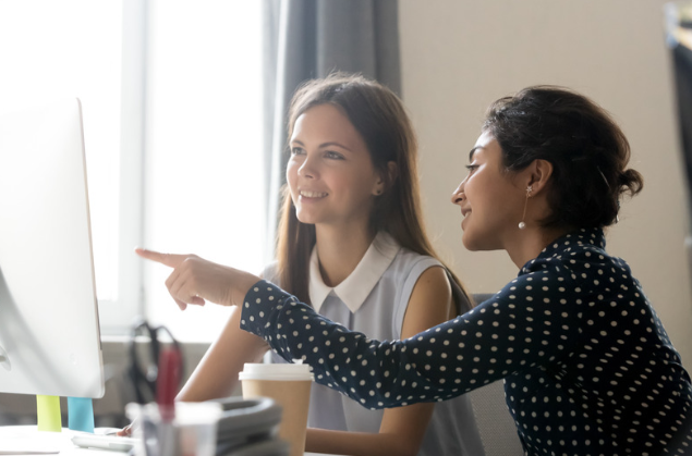 Two women sit looking at a computer screen.