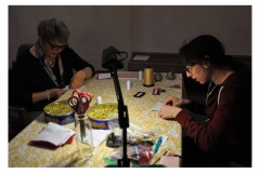 Artist Teresa Vander Meer-Chassé beading at table with guest.