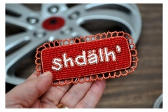 Close up of beaded badge with writing “shdälh'” on red and orange beaded border by artist Teresa Vander Meer-Chassé.